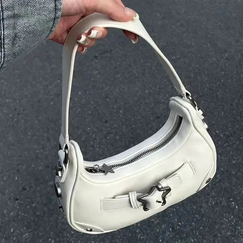 Une main montre le sac fourre-tout à bandoulière Drips-Way Vintage Korean White Star, un joli sac à main zippé en cuir microfibre avec des accents d'étoiles - un choix accrocheur et tendance pour les femmes qui se démarque sur un fond gris et un haut assorti.