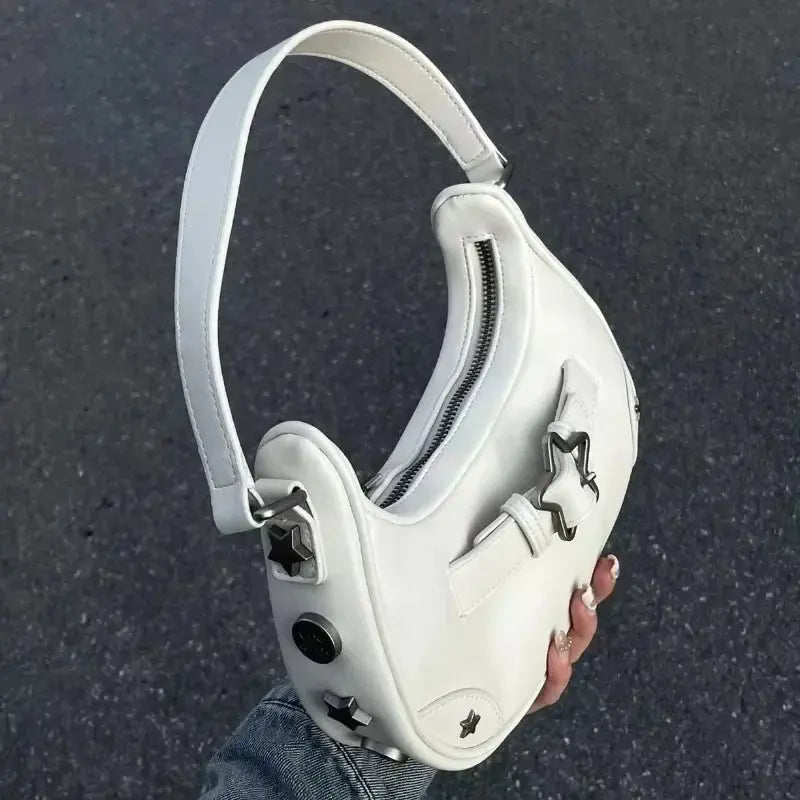 Une main tient le sac fourre-tout à bandoulière Drips-Way Vintage Korean Casual Cute White Star, fabriqué en cuir synthétique avec des clous en étoile argentés, une large bandoulière et une fermeture éclair sur le dessus - un accessoire tendance pour les looks mode féminins.