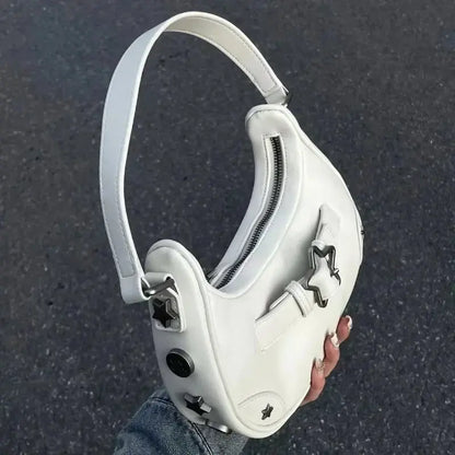 Une main tient le sac fourre-tout à bandoulière Drips-Way Vintage Korean Casual Cute White Star, fabriqué en cuir synthétique avec des clous en étoile argentés, une large bandoulière et une fermeture éclair sur le dessus - un accessoire tendance pour les looks mode féminins.