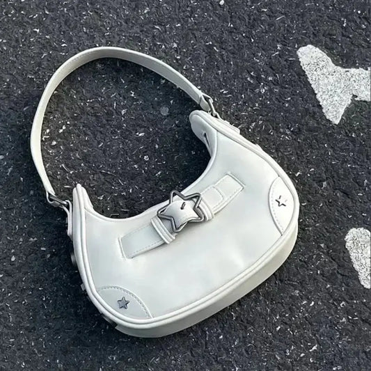 Le sac fourre-tout à bandoulière vintage coréen mignon en forme d'étoile blanche pour femme Drips-Way, fabriqué en cuir synthétique avec un détail en étoile et une poignée courte, repose avec style sur une surface texturée en asphalte foncé avec des marques blanches.